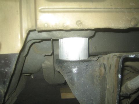 1990 Ford Bronco - Close-up of a shiny bare aluminum body-mount spacer puck installed under a truck cab.