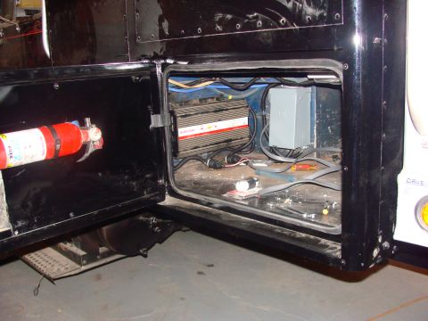 1992 Ford Bronco - A storage compartment on a vehicle is open, revealing electrical components and a fire extinguisher inside.