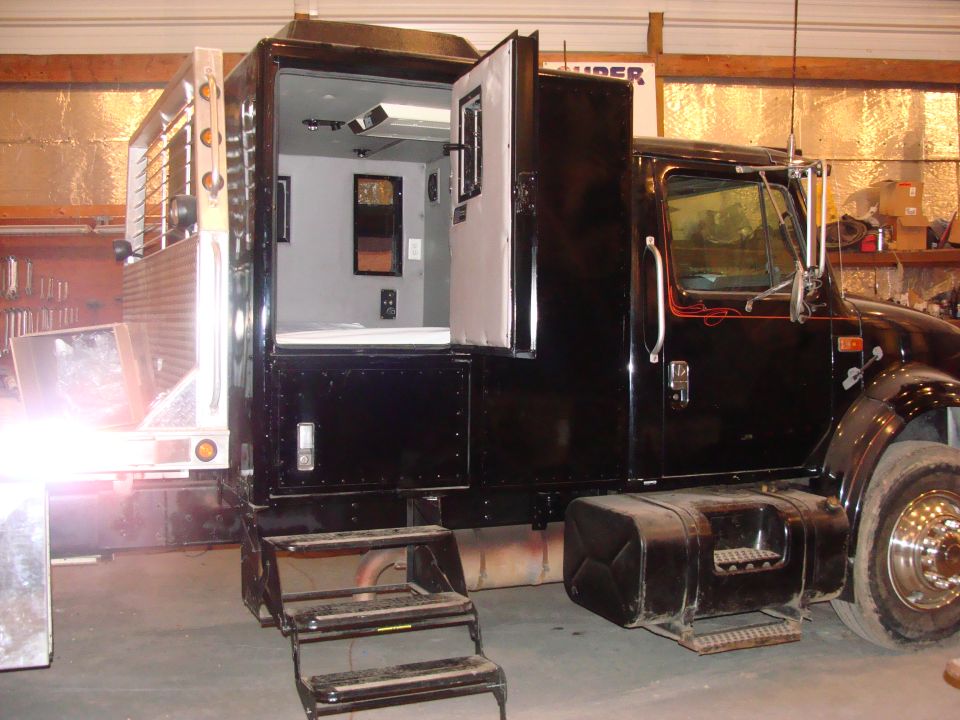 Black truck with a custom living space built into the back, doors open showing interior