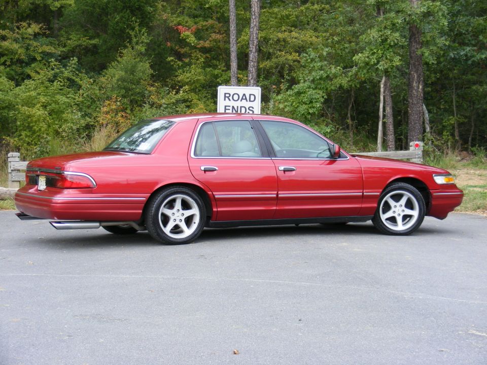 Red Mercury Grand Marquis sedan in profile on lowered aftermarket alloy wheels