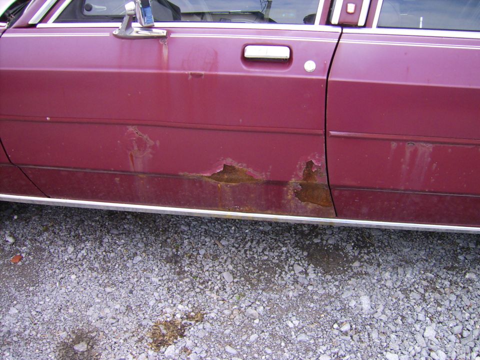 maroon sedan door showing significant rust damage along the lower body panel and trim