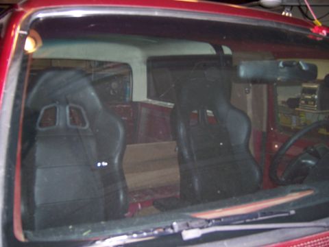 1991 Ford Bronco - The interior of a red vehicle is visible through the windshield, two black racing seats and wooden paneling in the rear.