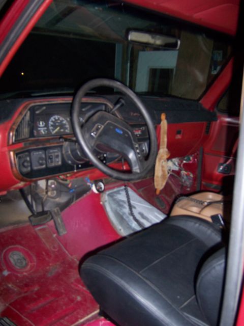 1991 Ford Bronco - The interior of a red truck cab, a dashboard, steering wheel, and seats. The dashboard has a Ford logo.