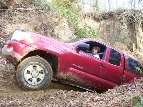2007 Jeep Wrangler - Red Toyota Tacoma pickup truck stuck in a muddy ditch off-road.