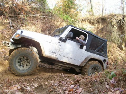 2007 Jeep Wrangler - A silver Jeep Wrangler navigates a challenging off-road trail with a driver visible inside.