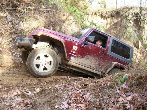 2007 Jeep Wrangler - A red 2007 Jeep Wrangler navigates a steep, muddy incline during an off-road excursion.