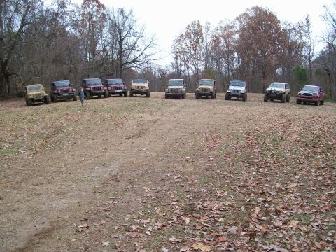 2007 Jeep Wrangler - A group of SUVs and trucks are parked in a wooded area on a cloudy day.