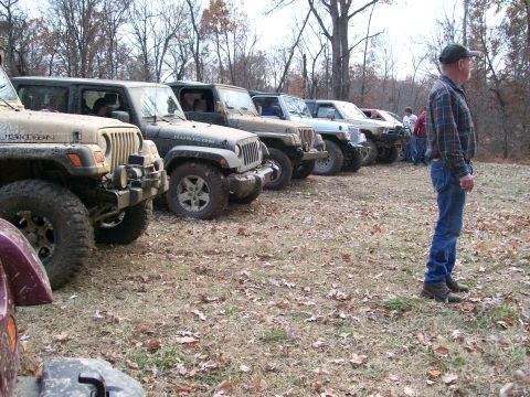 2007 Jeep Wrangler - Several Jeep Wranglers are parked in a line on a field with fallen leaves, with a man standing to the right observing.