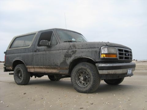 1994 Ford Bronco - A muddy 1992 Ford Bronco sits on a beach under an overcast sky.