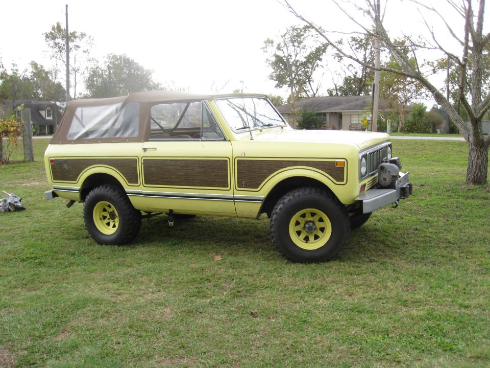 Yellow International Harvester Scout II with wood paneling and a brown soft top, parked on grass