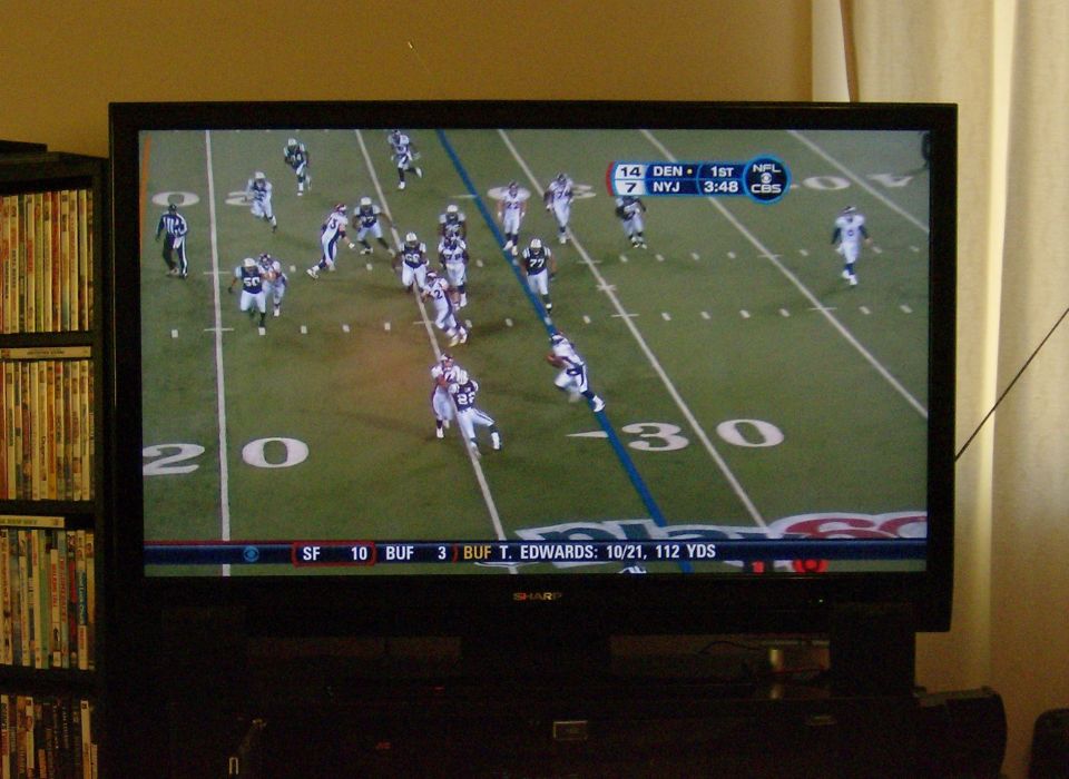 Television screen displaying a football game with score and player stats