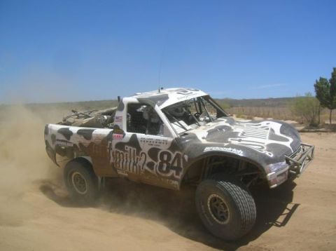 2008 Ford Bronco - A custom off-road truck races on a dusty track under a clear blue sky.