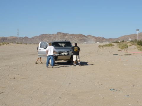2008 Ford Bronco - A desert scene with two men near a modified truck and another vehicle with an open door.