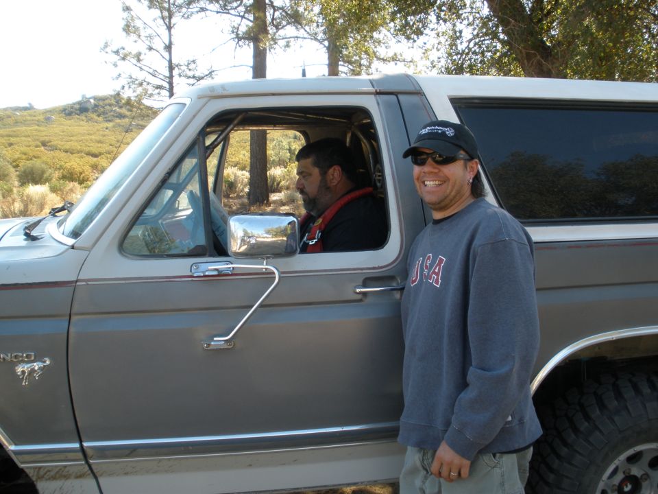 Gray Ford Bronco with a white roof, two men standing outside and inside, off-road tires visible