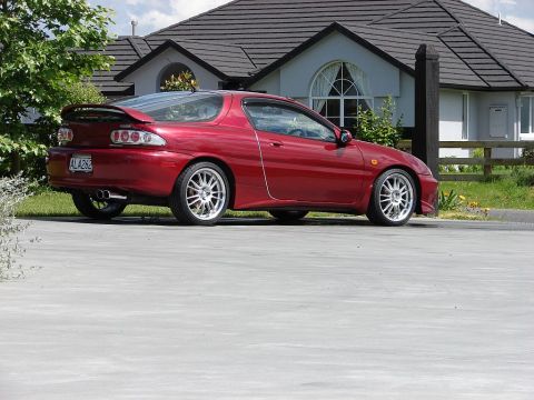 1993 Mazda MX-3 - This 1993 Mazda MX-3 coupe features a distinctive rear spoiler and sporty alloy wheels, captured in a side profile view.