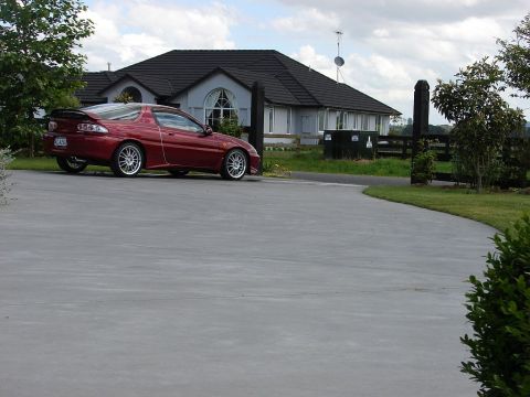 1993 Mazda MX-3 - A red 1993 Mazda MX-3 is parked on a concrete driveway with a house in the background.