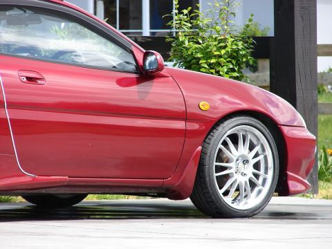 1993 Mazda MX-3 - Side profile of a red 1993 Mazda MX-3, focusing on the front quarter panel and door.
