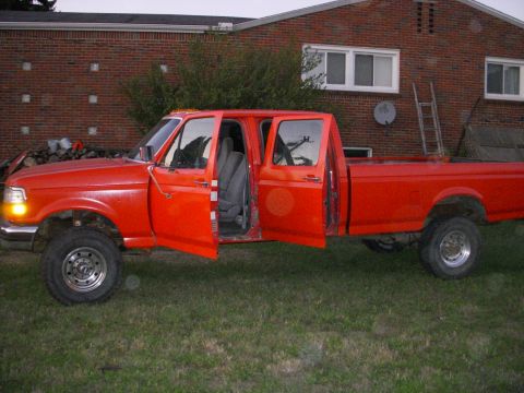 1992 Ford F-350 - This red pickup truck has four doors and is parked outside a brick building.