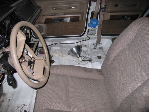 1991 Ford LTD Crown Victoria - Vehicle interior mid-restoration showing a tan steering wheel, dashboard and bare painted floor pan beside a cloth seat.