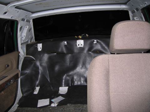 1991 Ford LTD Crown Victoria - Rear interior of a sedan with the black headliner backing exposed and clips visible, beside a tan cloth seat.