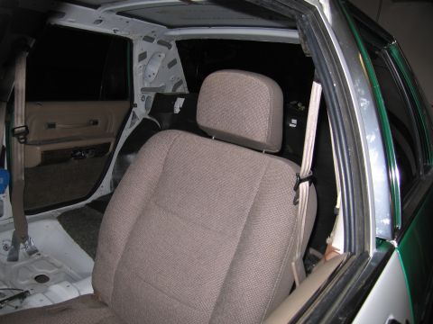 1991 Ford LTD Crown Victoria - Stripped sedan interior with a tan cloth front seat, exposed B-pillar and seat-belt anchor under restoration.