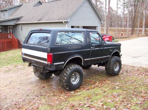 1992 Ford Bronco - A lifted black Ford Bronco with large tires sits in a driveway next to a house.