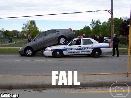 Gray sedan is on top of a police car. Several officers are standing around