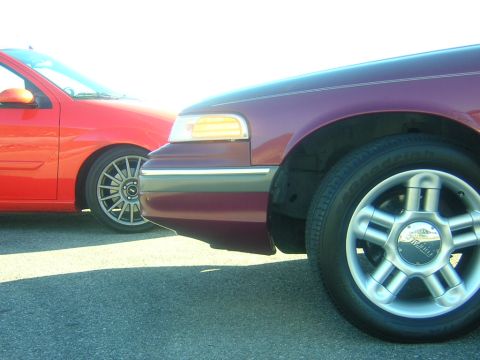 1992 Ford Crown Victoria - A maroon 1992 Ford Crown Victoria is parked next to a red car, showing the front quarter panel and wheel.