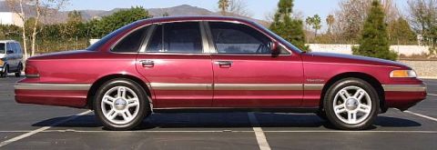 1992 Ford Crown Victoria - Side profile of a red 1992 Ford Crown Victoria sedan parked in a lot, with another vehicle visible in the background.
