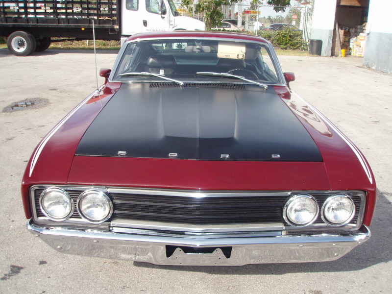 Front view of a red coupe with a black hood. Grille has horizontal bars. Dual headlights on each side