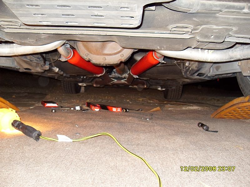 Under-car view of dual exhaust with red glasspack mufflers around the rear differential during install