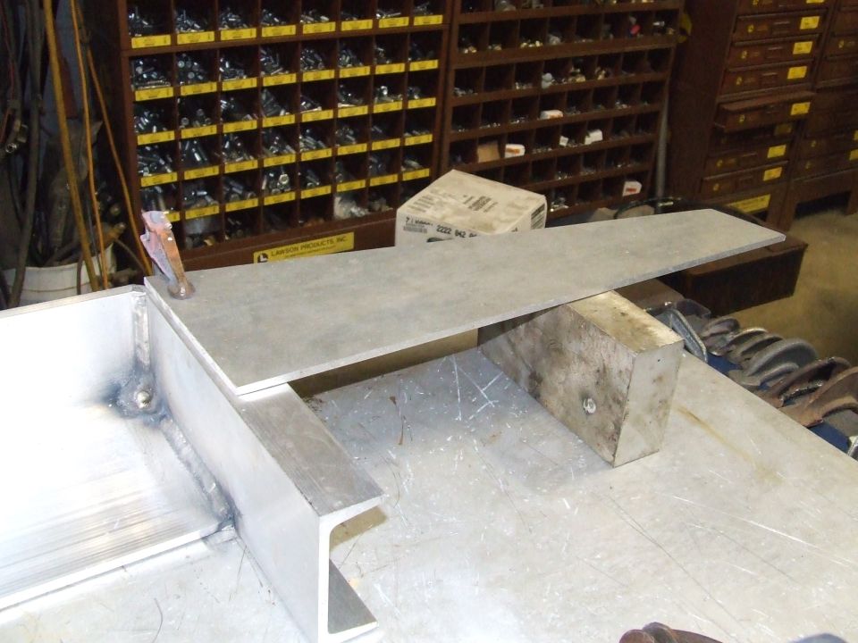 Metal pieces clamped and welded together on a workbench with a parts organizer in the background