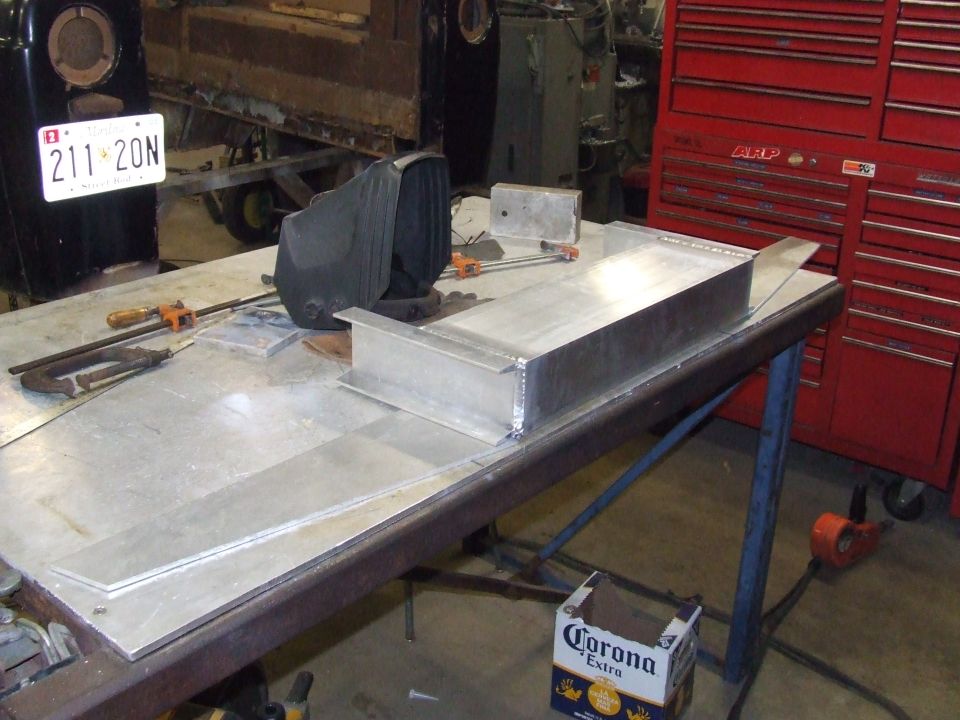 Aluminum parts on a workbench with a welding mask and red tool chest in background. License plate visible