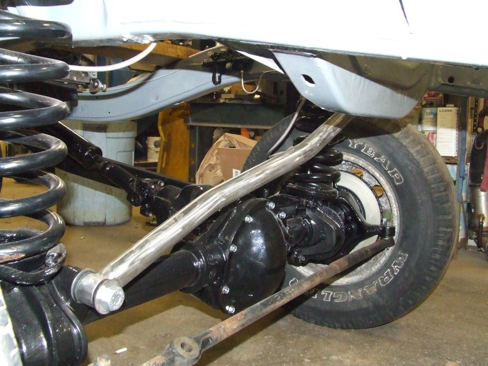 Close-up of a vehicle's rear axle, differential, springs, and sway bar. Tire visible with 'YEAR' and 'WRANGLER' text