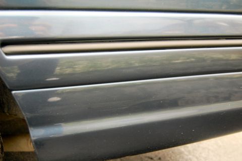1985 Mercury Grand Marquis - Close-up of the side trim on a vehicle, showing horizontal lines and a dark accent strip.