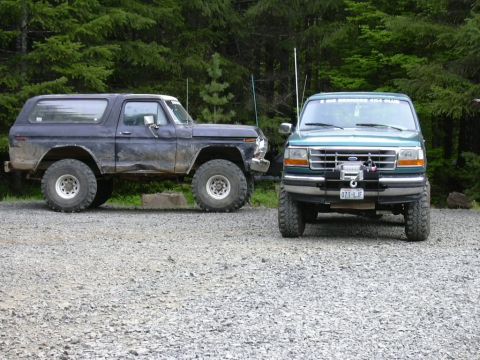 1991 Ford Bronco - Two Ford trucks are parked on a gravel lot with trees in the background.