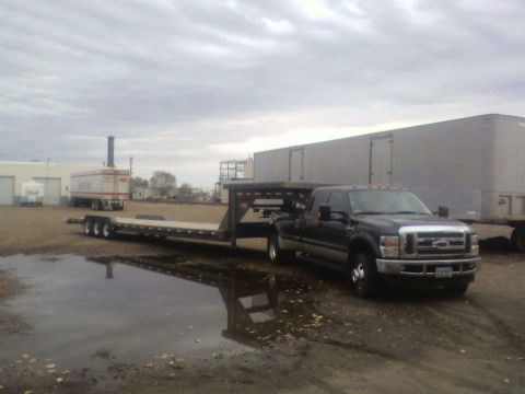 1992 Ford F-350 - A dark-colored Ford F-series truck is hitched to a gooseneck trailer in a lot with puddles.