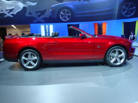 1993 Ford Taurus - A red convertible is displayed at an auto show with other vehicles and graphics in the background.
