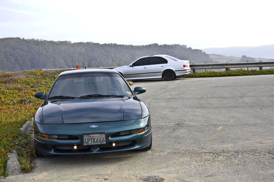 Green 1996 Ford Probe parked on the side of the road with a silver BMW sedan behind it