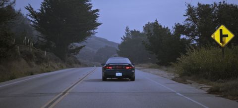 1996 Ford Probe - A black 1996 Ford Probe travels down a rural highway under a cloudy sky.