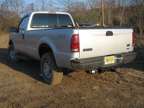 1990 Ford Bronco - Silver Ford F-250 pickup truck parked on dirt with trees in background.