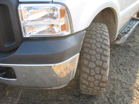 1990 Ford Bronco - Close-up of a truck's front fender, headlight, and tire. The vehicle has a chrome bumper and running boards.
