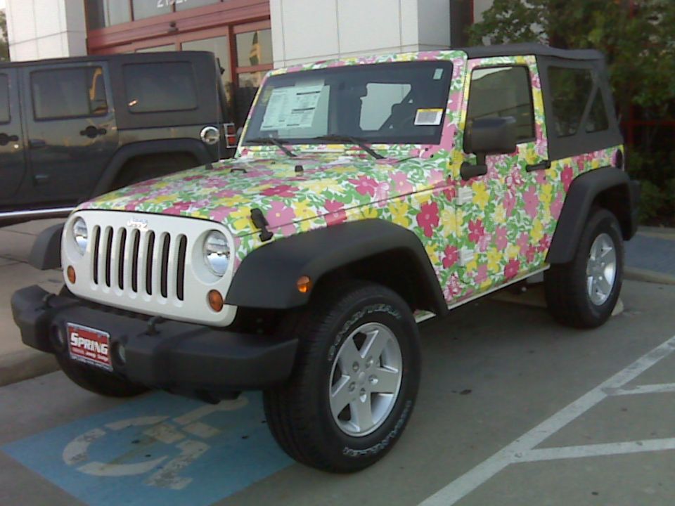 Floral-wrapped two-door Jeep Wrangler with black soft top parked at a dealership