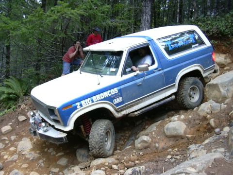 1991 Ford Bronco - This blue and white Ford Bronco navigates a challenging rocky trail, displaying "2 BIG BRONCOS" on its side.