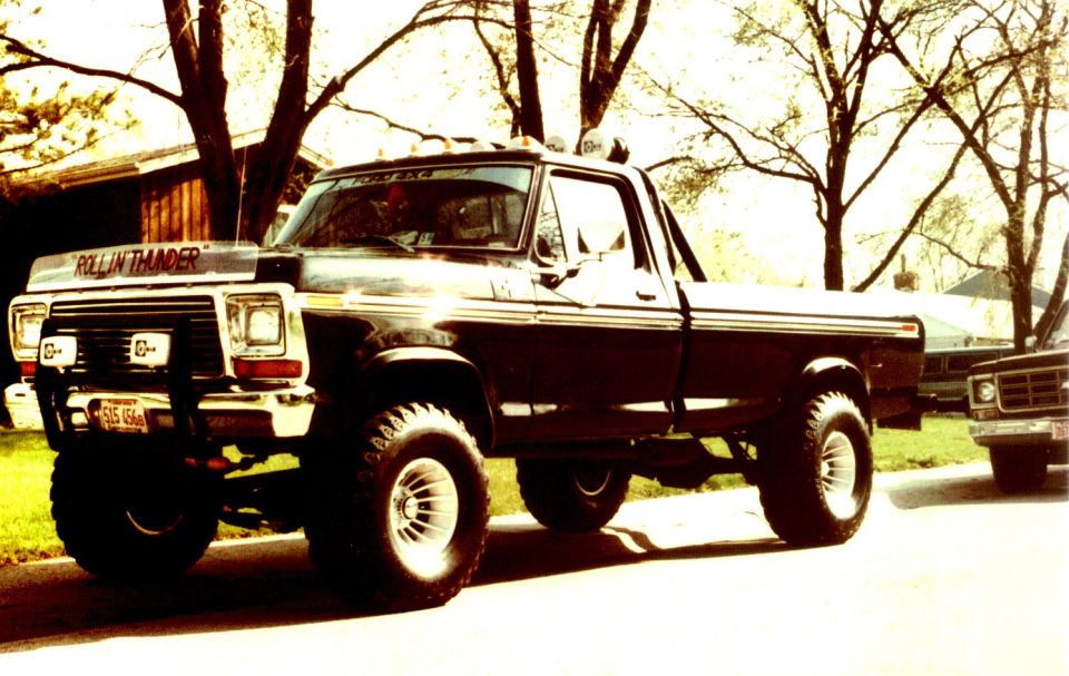 Black 1979 Ford F-150 pickup truck with "ROLLIN THUNDER" on the hood, lifted with large tires