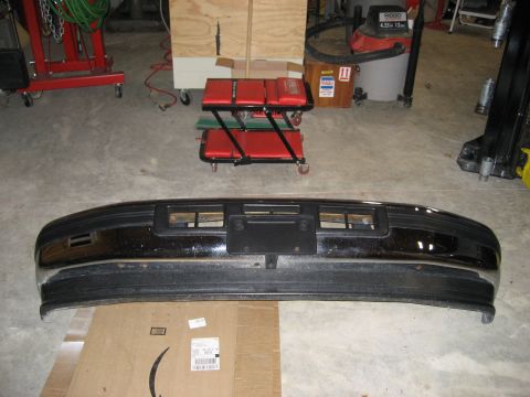 1996 Ford Bronco - A detached black front bumper with chrome accents and a license plate bracket is shown on the floor.