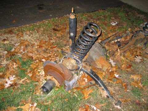1996 Ford Bronco - Vehicle suspension parts, including a shock and coil spring, lie on the ground covered in leaves.