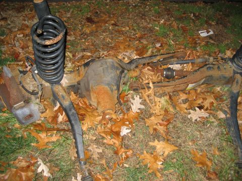 1996 Ford Bronco - Discarded vehicle suspension parts lie on the ground covered in fallen leaves.