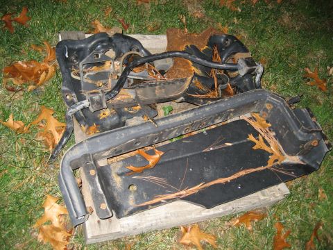 1996 Ford Bronco - Scrap metal parts, likely from a vehicle's front end, lie on a grassy area with fallen leaves.