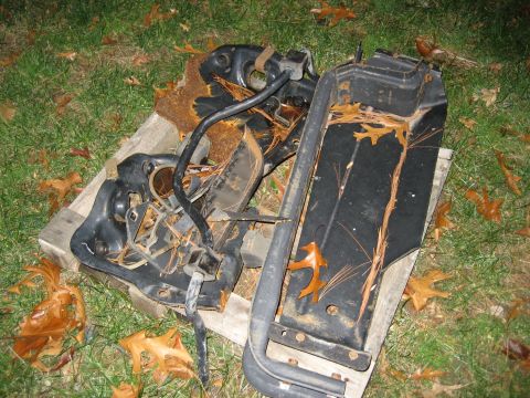 1996 Ford Bronco - Assorted rusted vehicle parts are piled on a wooden pallet in the grass, covered with leaves and pine needles.